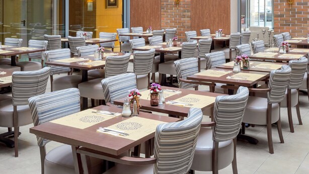 A spacious restaurant with high ceilings, mirrored spherical light fixtures, and a brick wall. Tables are set with striped chairs and centerpieces. - Marmara Hotel Budapest (Budapest)
