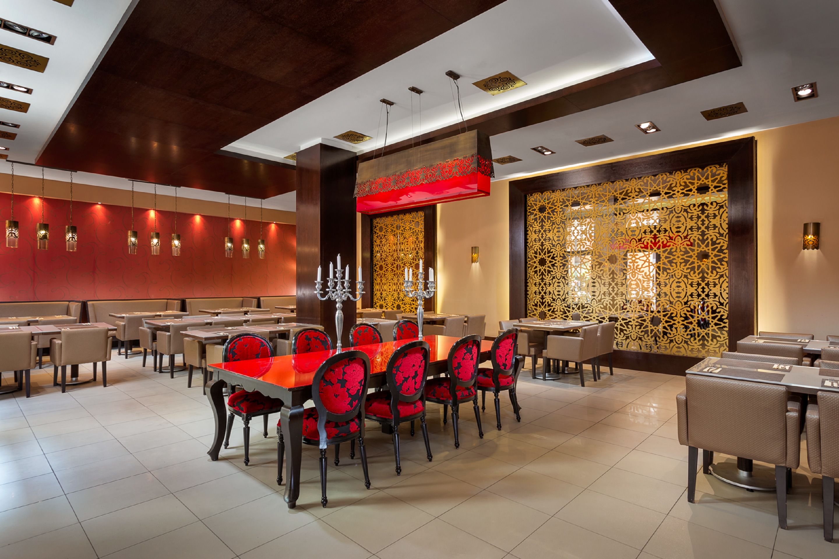 Un restaurant spacieux, doté de nombreuses tables et chaises, d’un mur décoratif orné de motifs complexes et d’un plafond au design moderne.