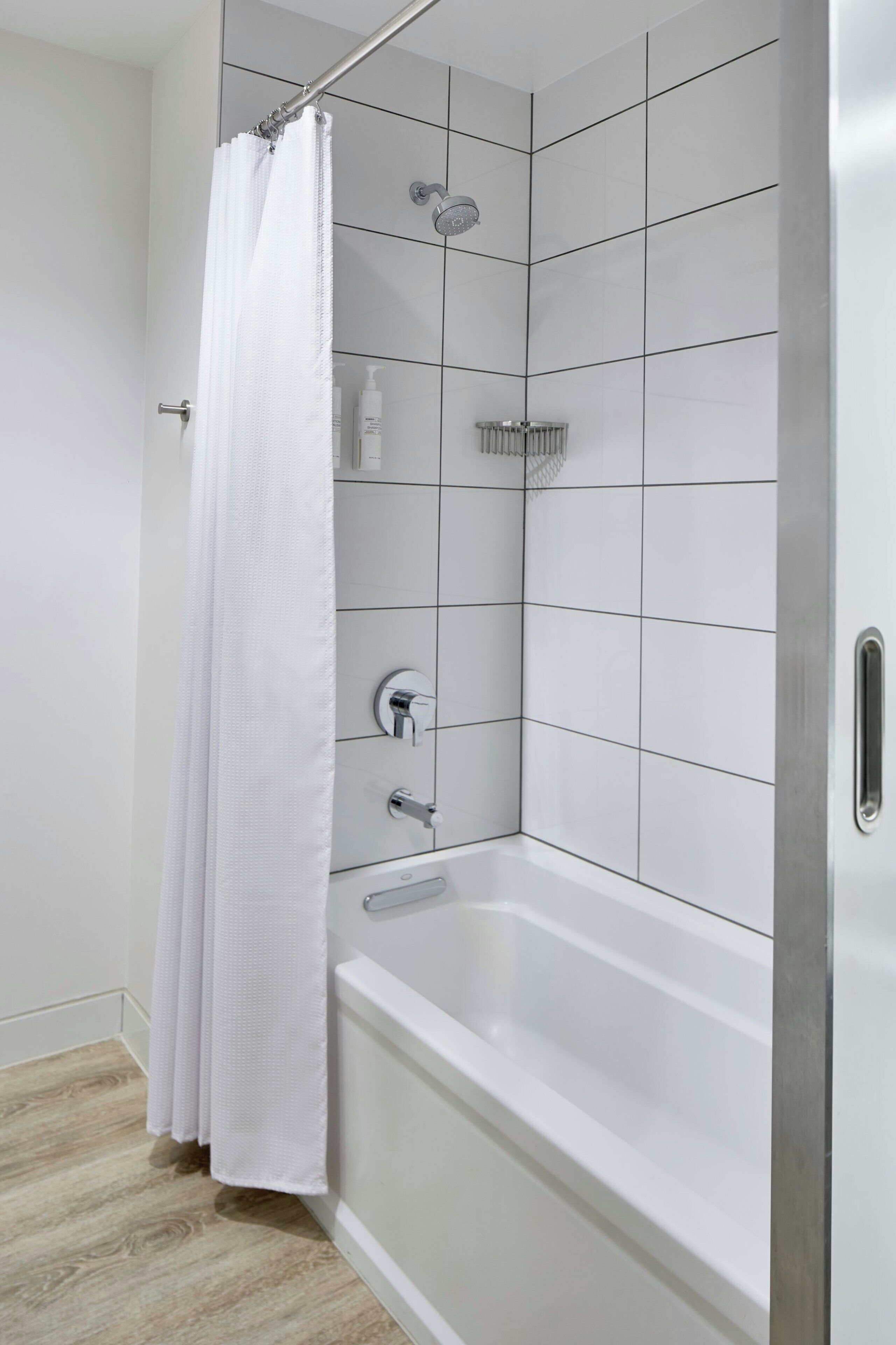 A modern bathroom with a white bathtub, a shower with a rain showerhead, and a white shower curtain.