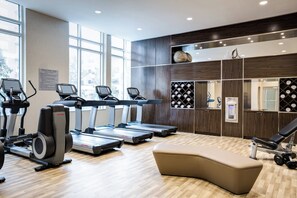 Ein Fitnessraum mit Laufbändern, einer Bank und einem an der Wand befestigten Weinkühler.