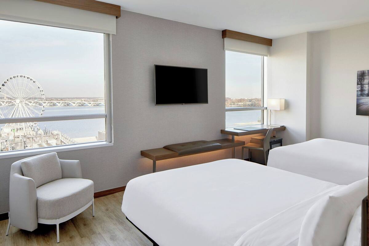 A hotel room with a bed, a desk, a chair, a TV, and a view of a Ferris wheel.