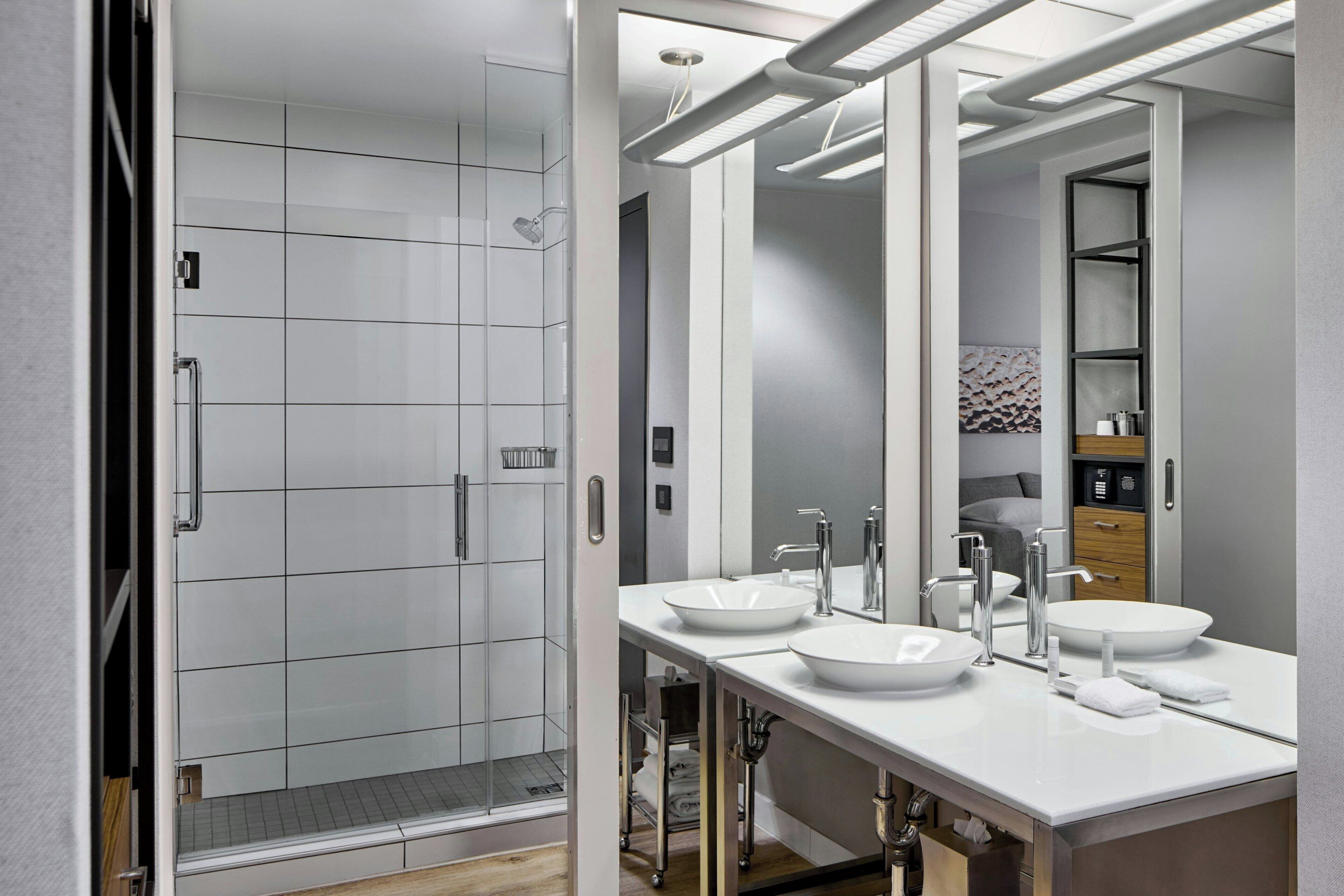 Un baño moderno con ducha a nivel del suelo, dos lavamanos y un espejo grande.