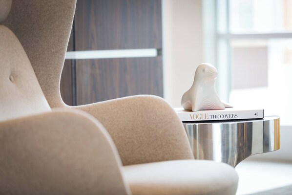 A modern chair with a metallic side table, a white decorative object, and a book titled "VOGUE THE COVERS" on the table.