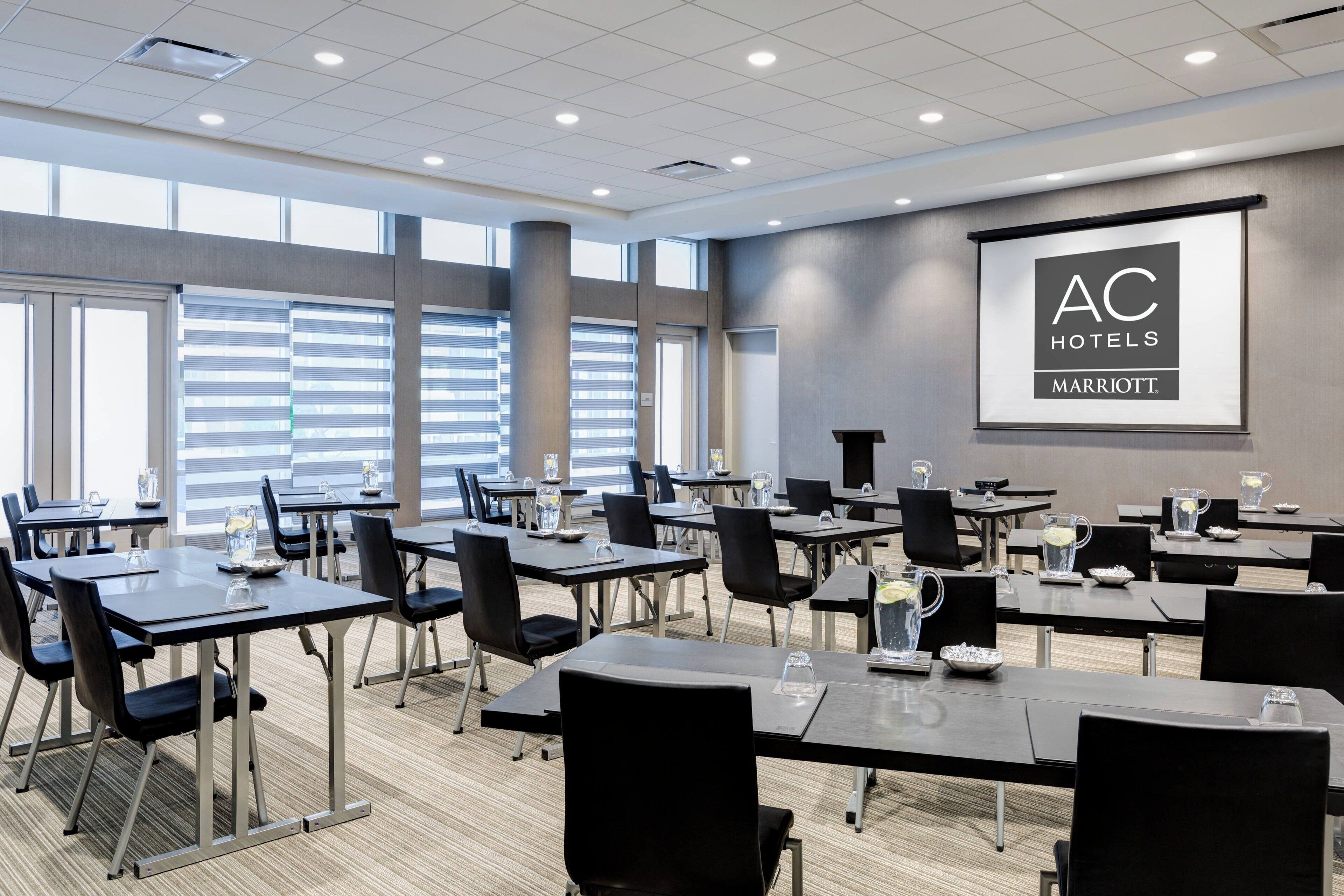Ett konferensrum med bord, stolar och en stor skärm som visar varumärket "AC Hotels Marriott".