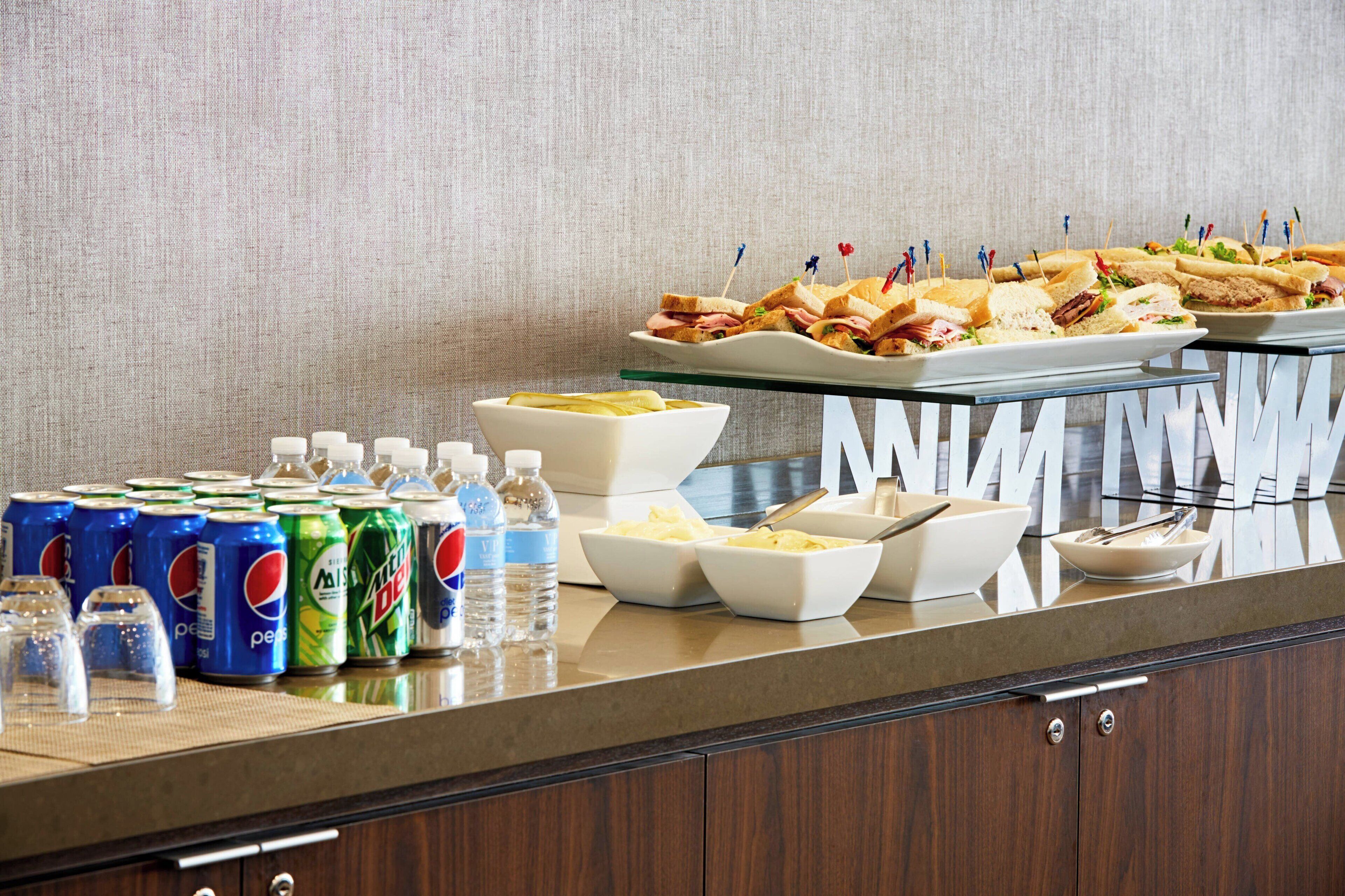 Una mesa de buffet con sándwiches, tazones de papas fritas y bebidas, incluyendo Pepsi y Mountain Dew.