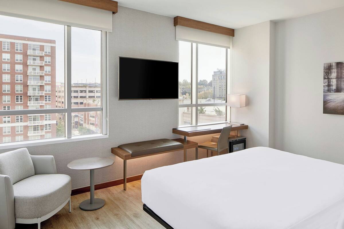 A hotel room with a large bed, a desk with a chair, a small round table, and a TV mounted on the wall.