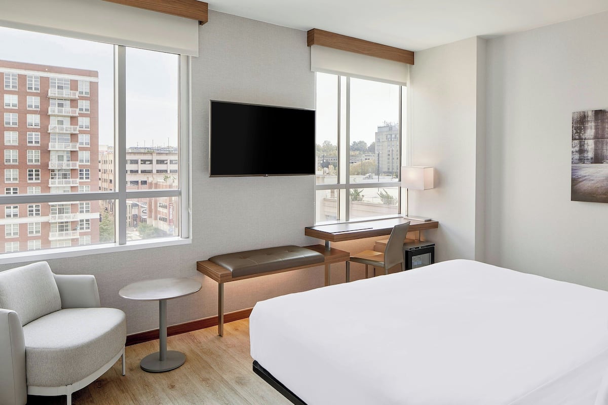 Une chambre d’hôtel avec un grand lit, un bureau avec une chaise, une petite table ronde et un téléviseur fixé au mur.
