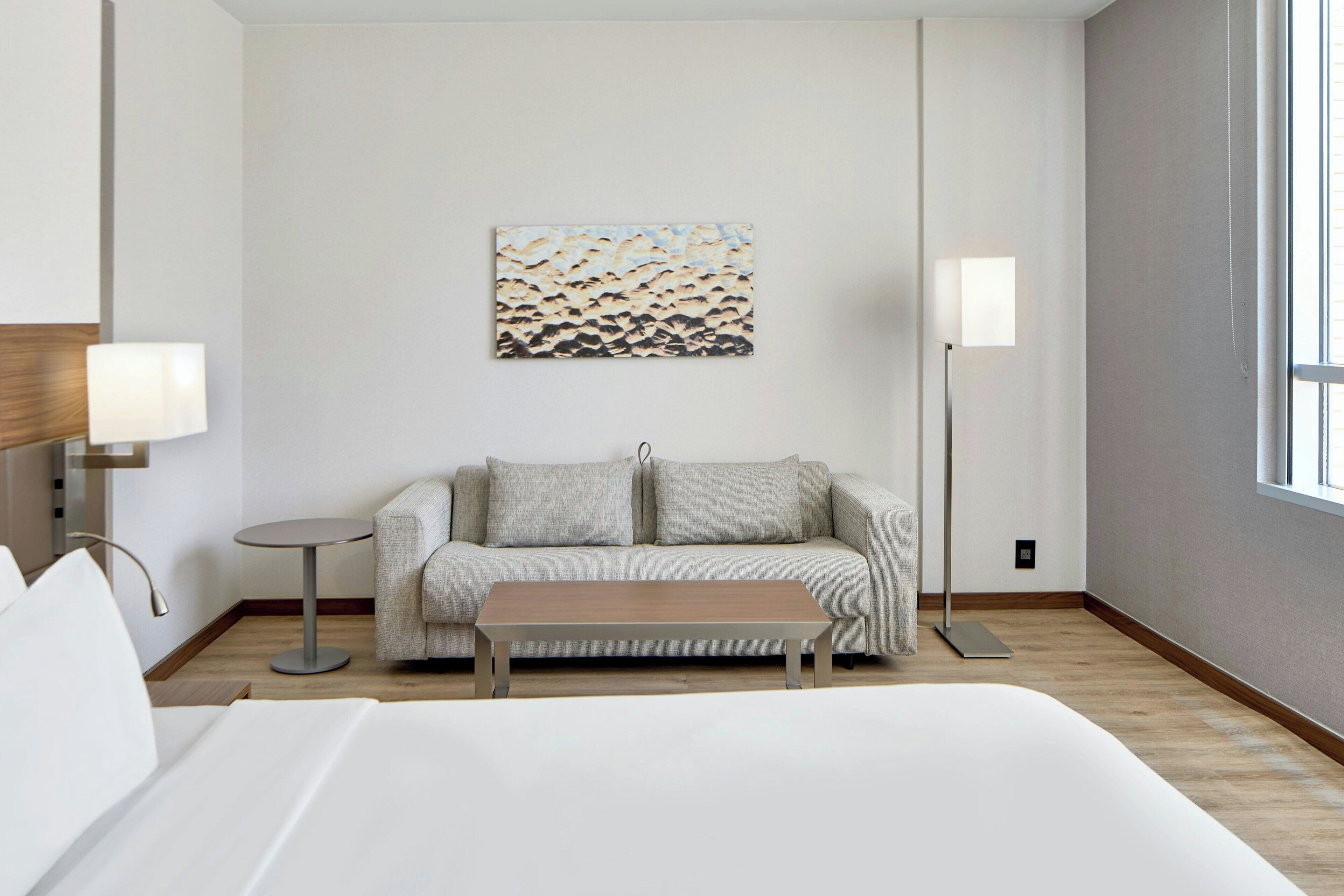 Habitación de hotel con una cama, un sofá, una mesa de centro, una lámpara, un cuadro y una lámpara de pie.