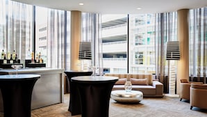 Un área lounge moderna con bar, asientos y amplios ventanales que ofrecen vistas a la ciudad.