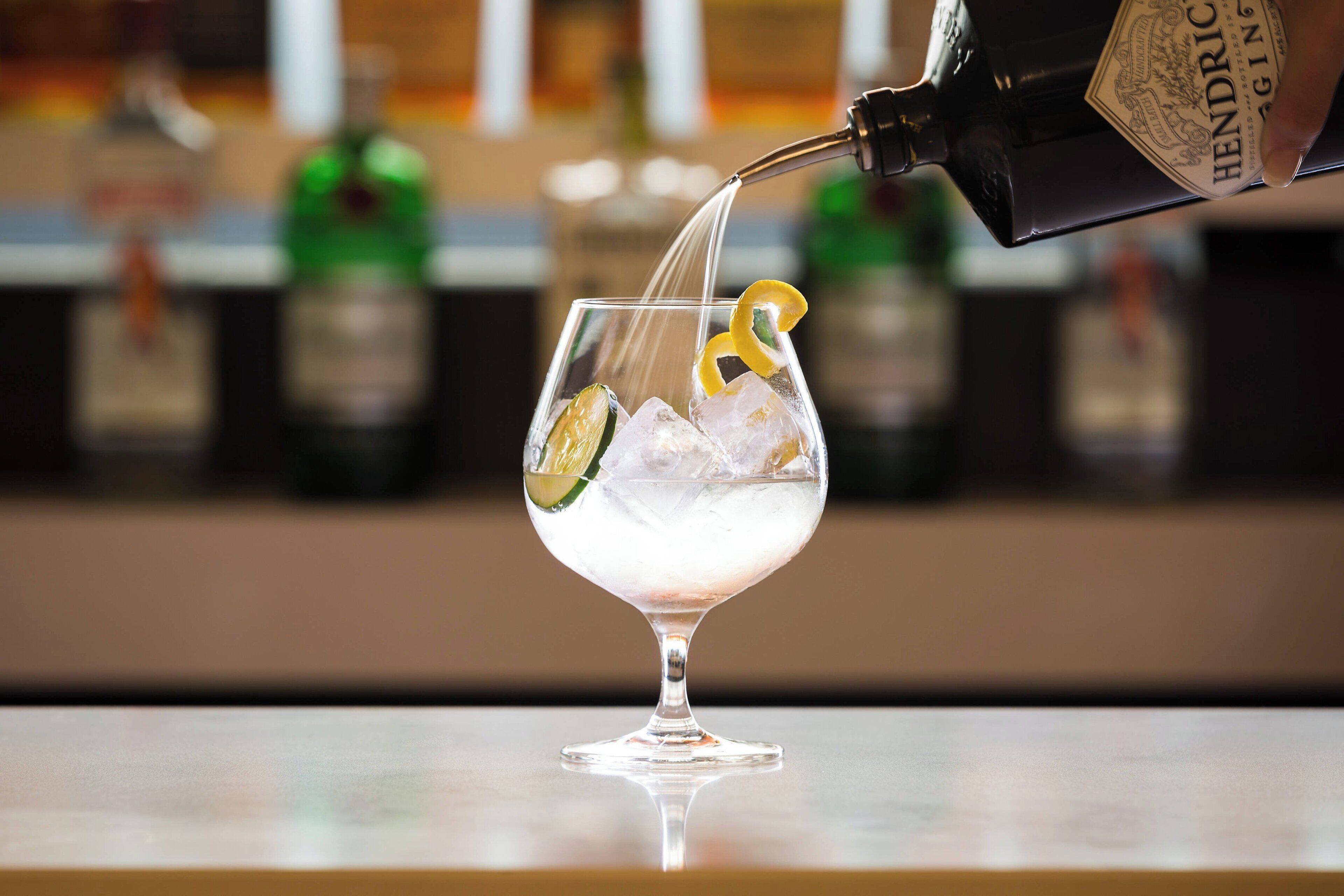 Ein Cocktail wird in ein Glas mit Eis und Zitrusfrüchten eingefüllt.