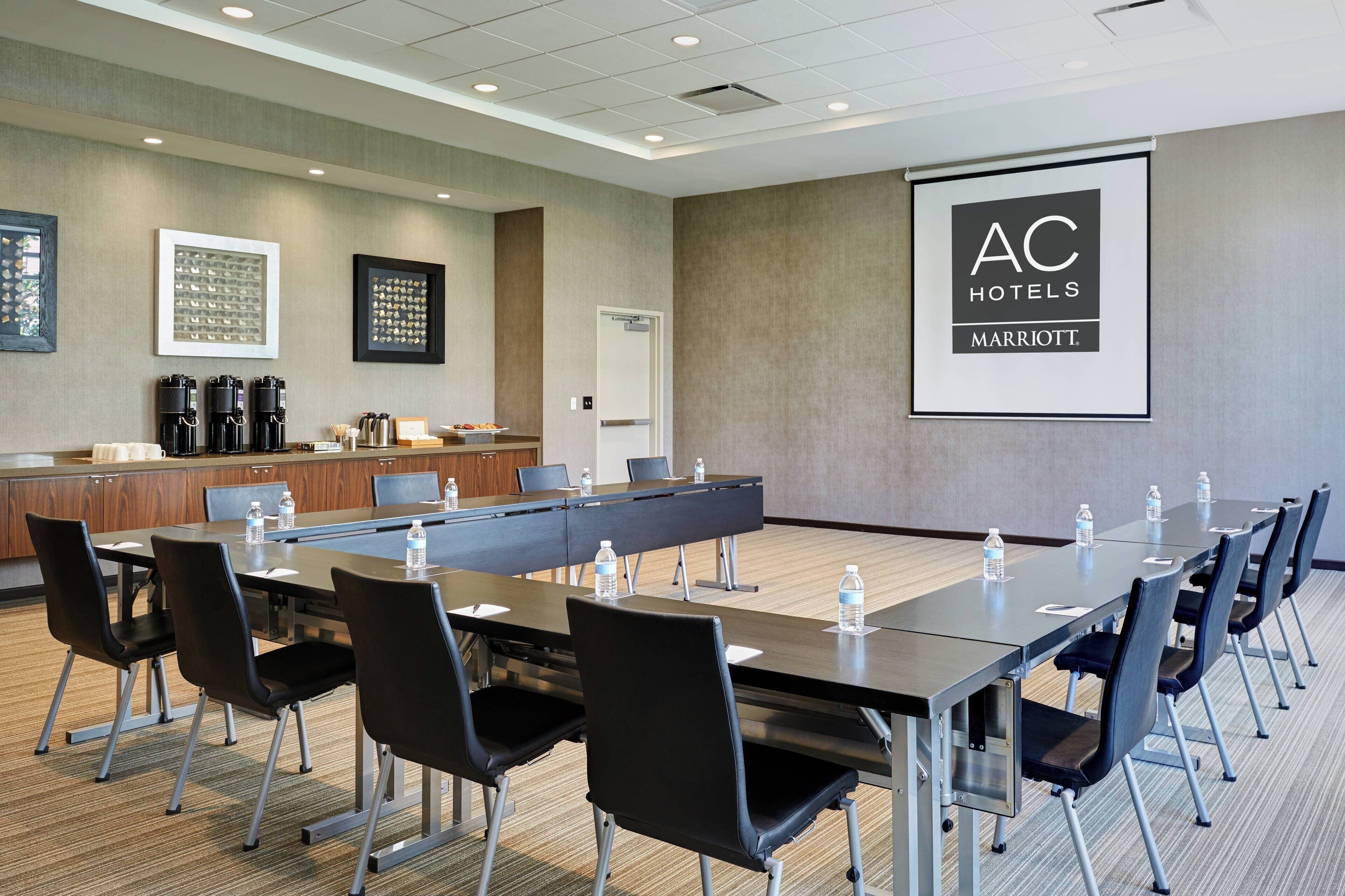 A conference room with a long table, black chairs, water bottles, and a coffee station.