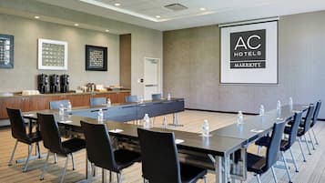 Un salón de conferencias con una larga mesa, sillas negras, botellas de agua y una estación de café.