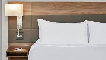 A neatly made bed with white linens, a wooden headboard, a bedside table with a lamp, and a power outlet.