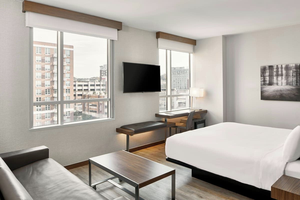 A hotel room with a bed, a desk, a chair, a sofa, and a TV.