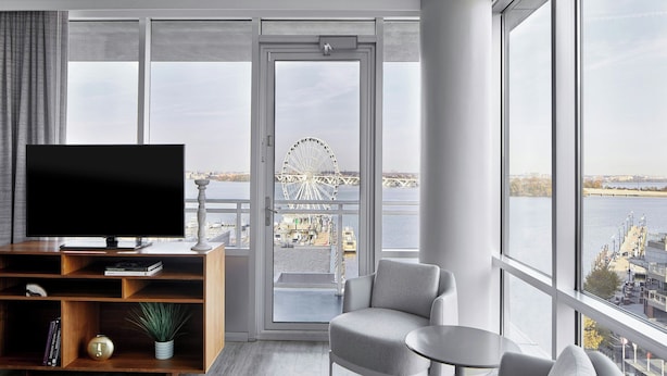 Una sala de estar moderna con un televisor grande, un mueble de entretenimiento de madera y una zona de estar con vista a una noria y al agua.