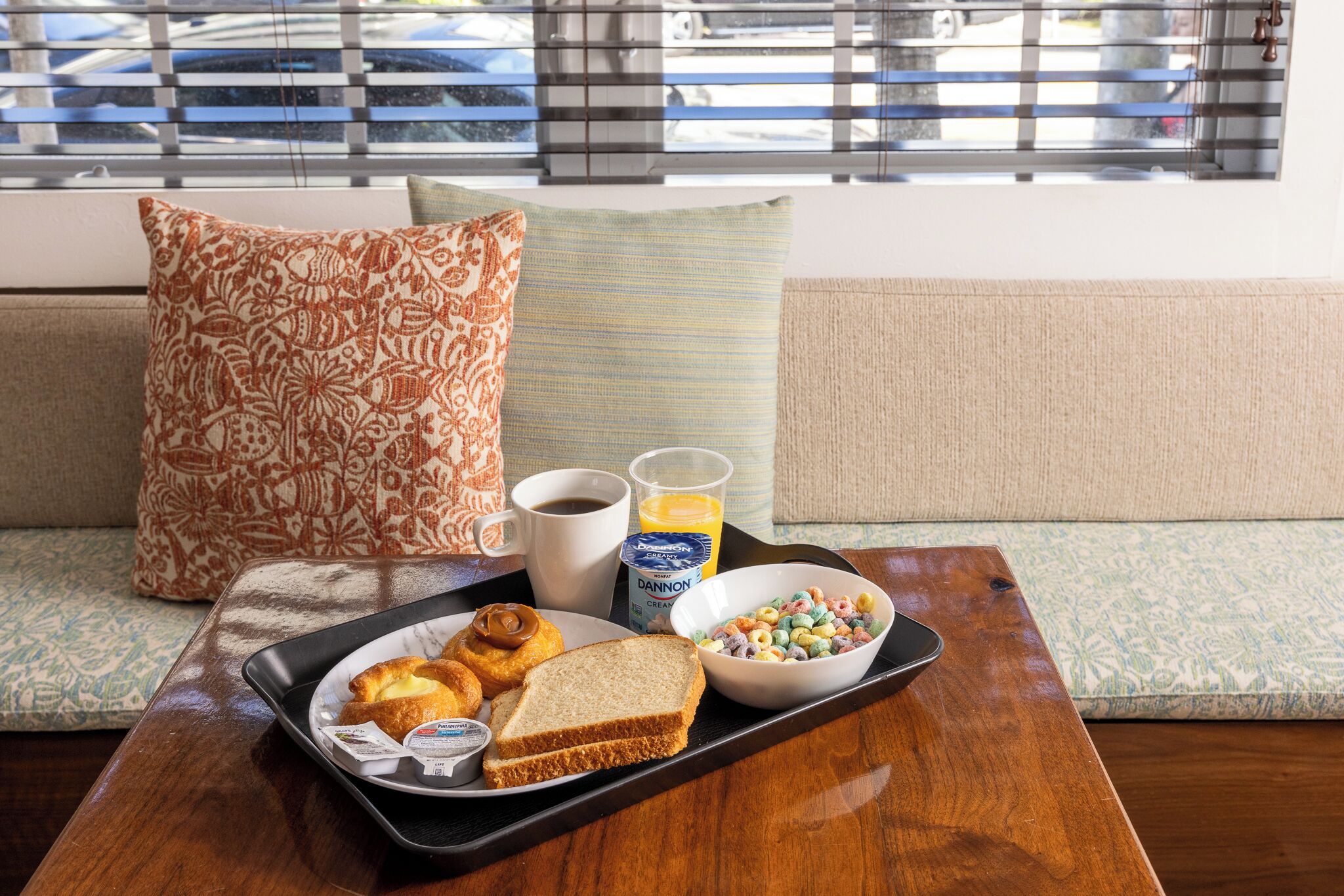 A breakfast tray on a wooden table with croissants, a sandwich, a bowl of cereal, a coffee cup, and a juice glass.