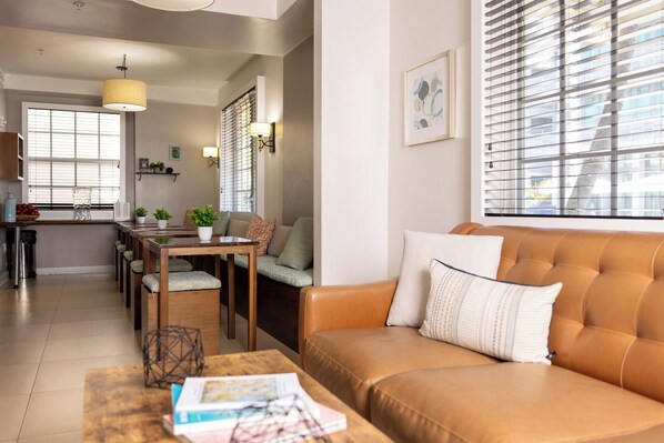 A modern living room with a brown leather sofa, a wooden coffee table, and a dining area with a table and chairs.