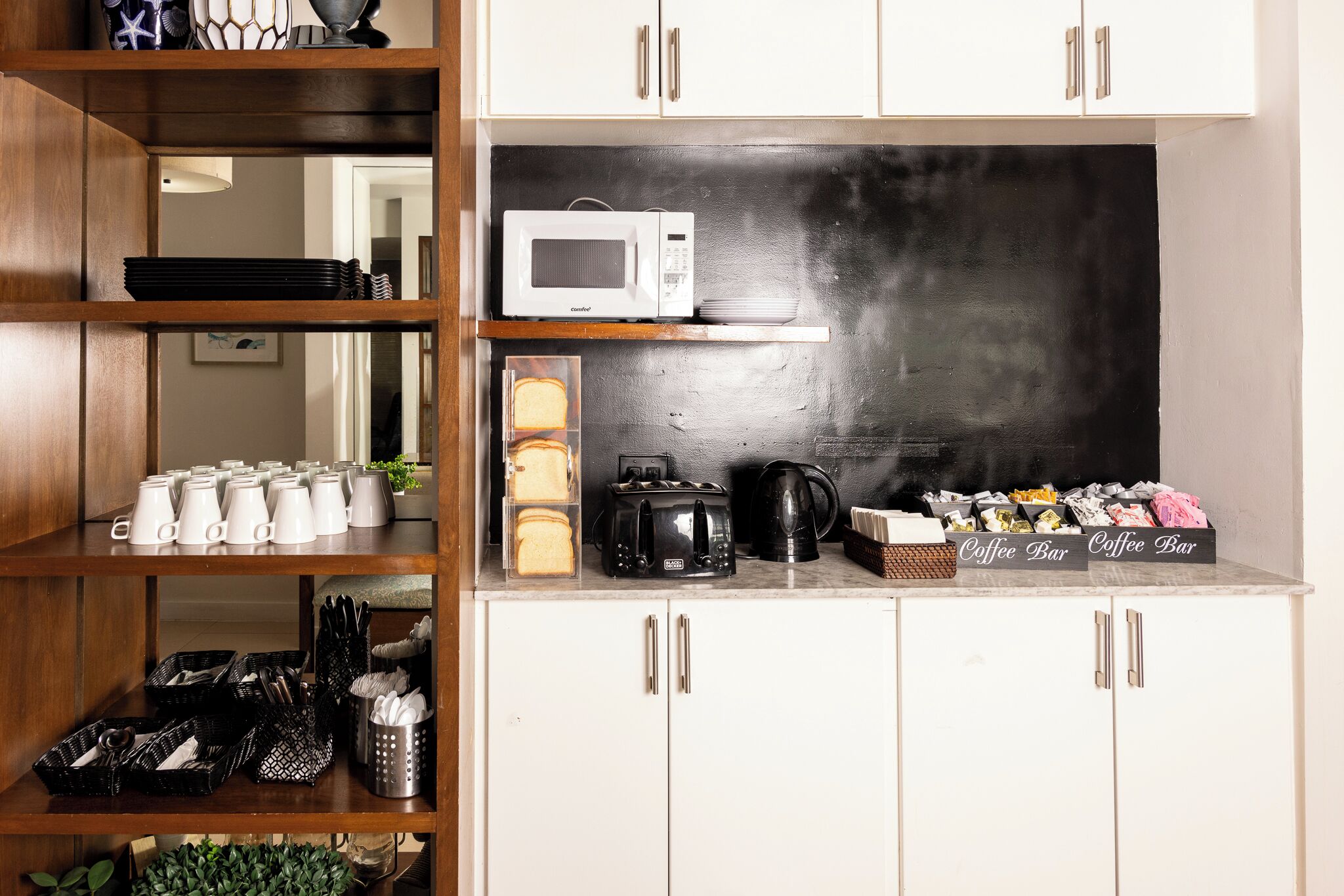 Una cocina con armarios blancos, microondas, tostadora y una barra para café.