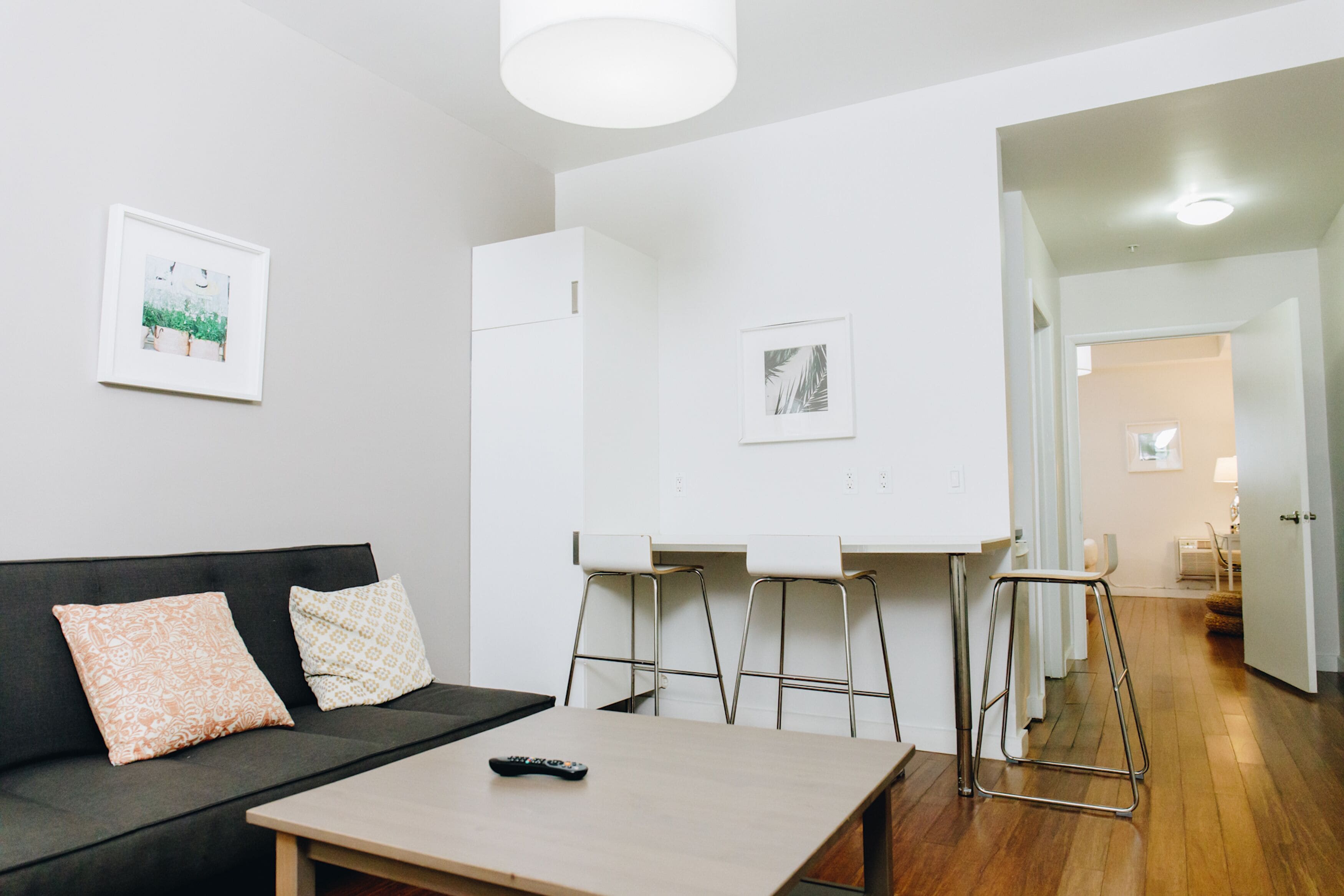 Un salon moderne comprenant un canapé, une table basse et un petit coin cuisine avec des tabourets.