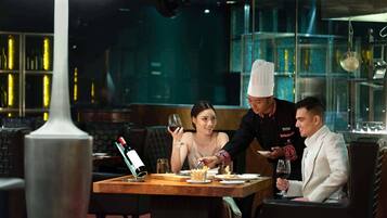 A restaurant setting with a table, chairs, a bottle of wine, and a person serving food.