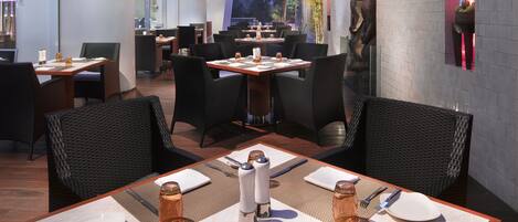 A restaurant with outdoor seating, tables set with white plates, silverware, and glasses, and a decorative salt and pepper shaker centerpiece.