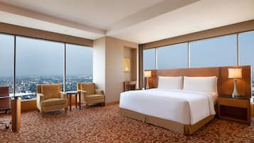 Un cuarto de hotel con una cama grande, dos sillones, un escritorio y vista a la ciudad.