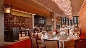 A spacious dining area with round tables set for multiple guests, featuring a red carpet and modern lighting fixtures.