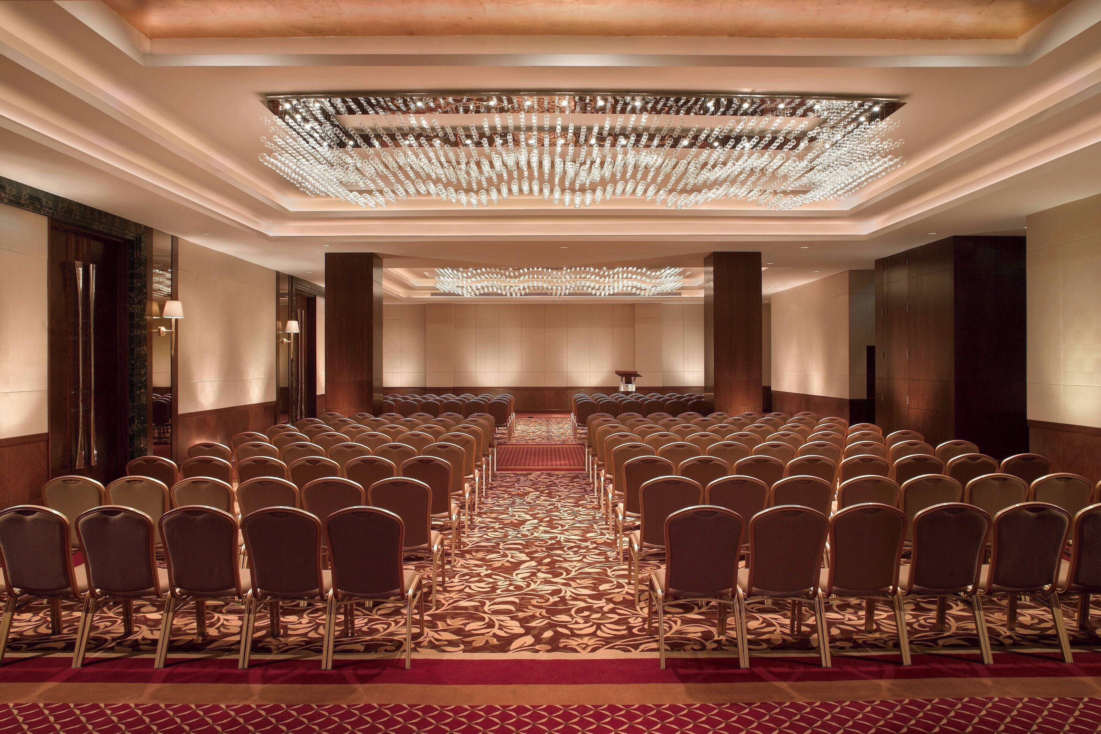 A conference room with rows of chairs, a patterned carpet, and a chandelier.
