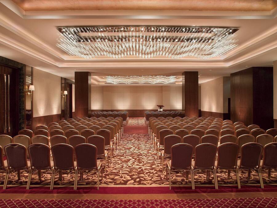 A conference room with rows of chairs, a patterned carpet, and a chandelier.