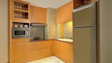 Cocina compacta con armarios de madera, microondas integrado y refrigerador de acero inoxidable.