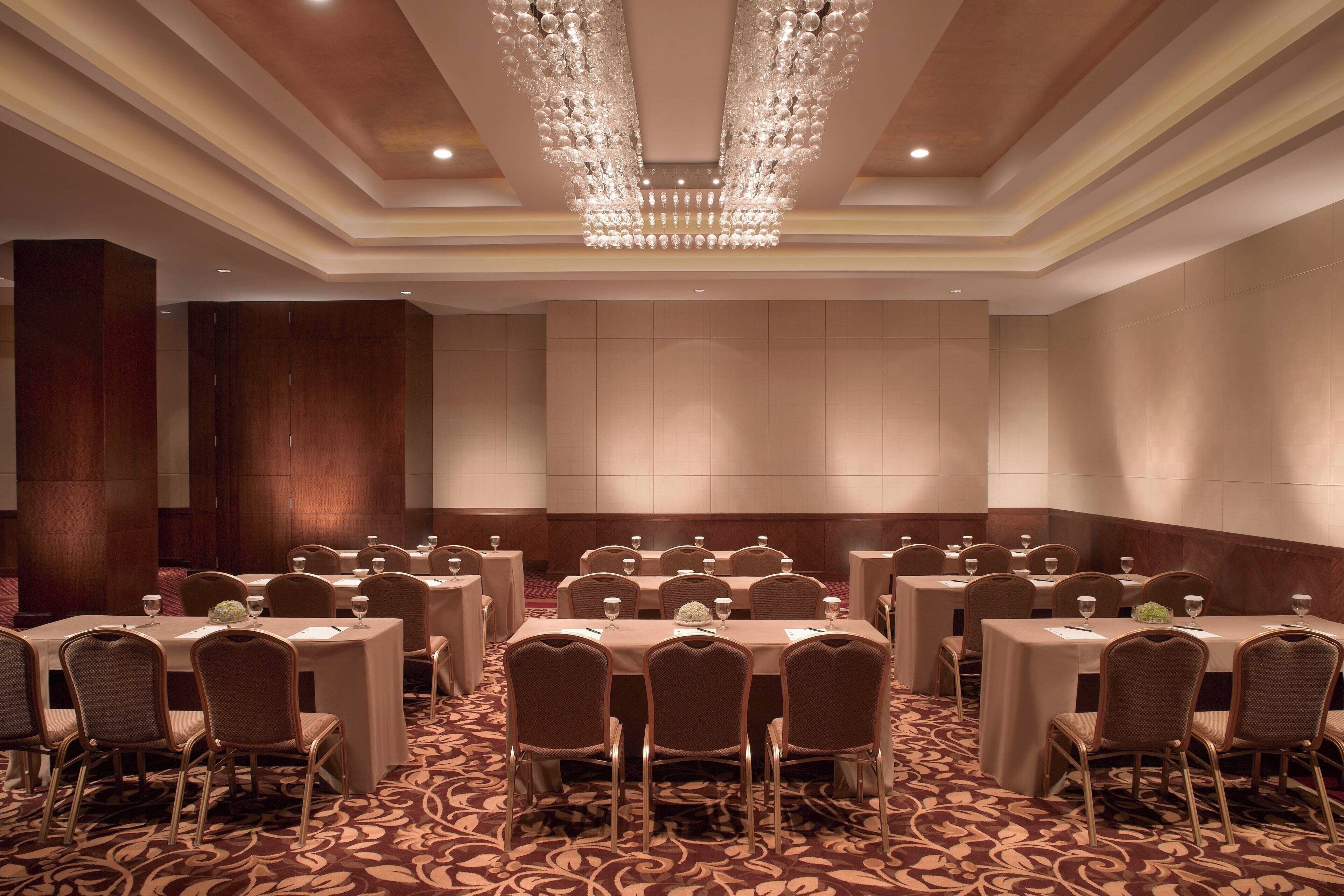 A conference room with multiple tables and chairs, a chandelier, and a patterned carpet.