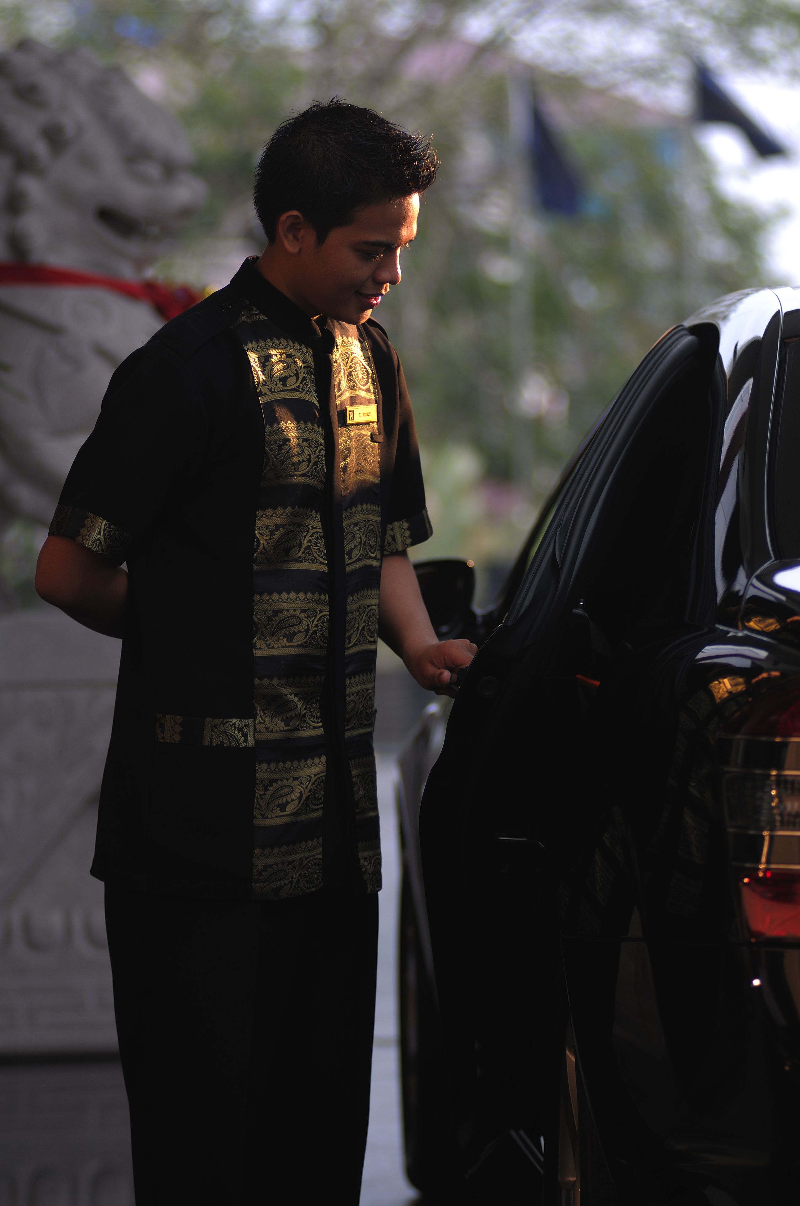 Una persona de pie al lado de un automóvil, usando una camisa estampada.