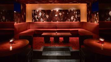 Ein schwach beleuchteter Raum mit einem rot gepolsterten Sofa, einem Holztisch und einer Wand mit Muster.
