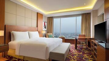 A hotel room with a large bed, a TV, a desk, and a view of the city.