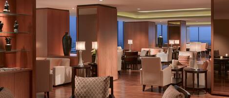 A spacious hotel lobby with multiple seating areas, including sofas and chairs, and a central dining table.