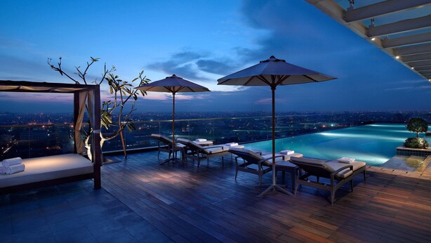 A rooftop terrace with lounge chairs, umbrellas, and a view of a cityscape at dusk. - JW Marriott Hotel Medan (Medan)