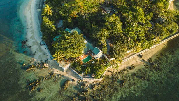 An aerial view of a tropical island with a beach, dense vegetation, and a single house with a swimming pool. - Hideaway Island Resort (Hideaway Island)