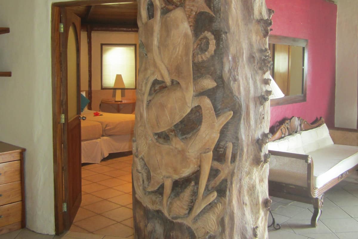 Une pièce comprenant une sculpture en bois, un lit, une table de chevet et une fenêtre avec des stores.