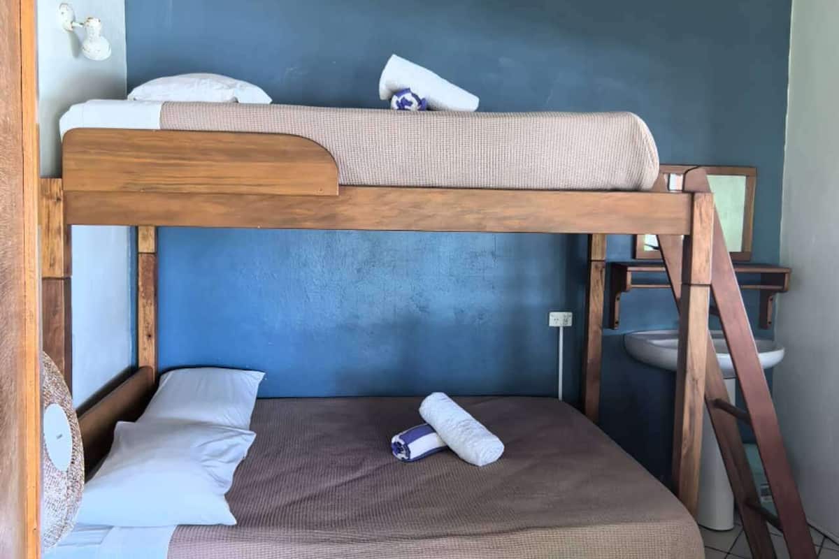 Un lit superposé avec une structure en bois, un mur bleu et un luminaire suspendu.