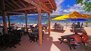 Un restaurante frente a la playa con terraza, techo de paja y vistas al mar.