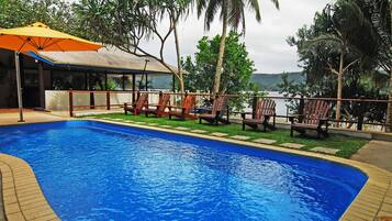 Una piscina al aire libre, sombrillas, sillones reclinables de piscina