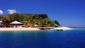 A beachside resort with a white sandy beach, clear blue water, and a lush green hill in the background. - Hideaway Island Resort (Hideaway Island)