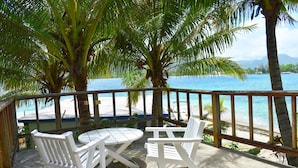 A beachside patio with white chairs and a table, overlooking a clear blue sea and a sandy beach. - Hideaway Island Resort (Hideaway Island)