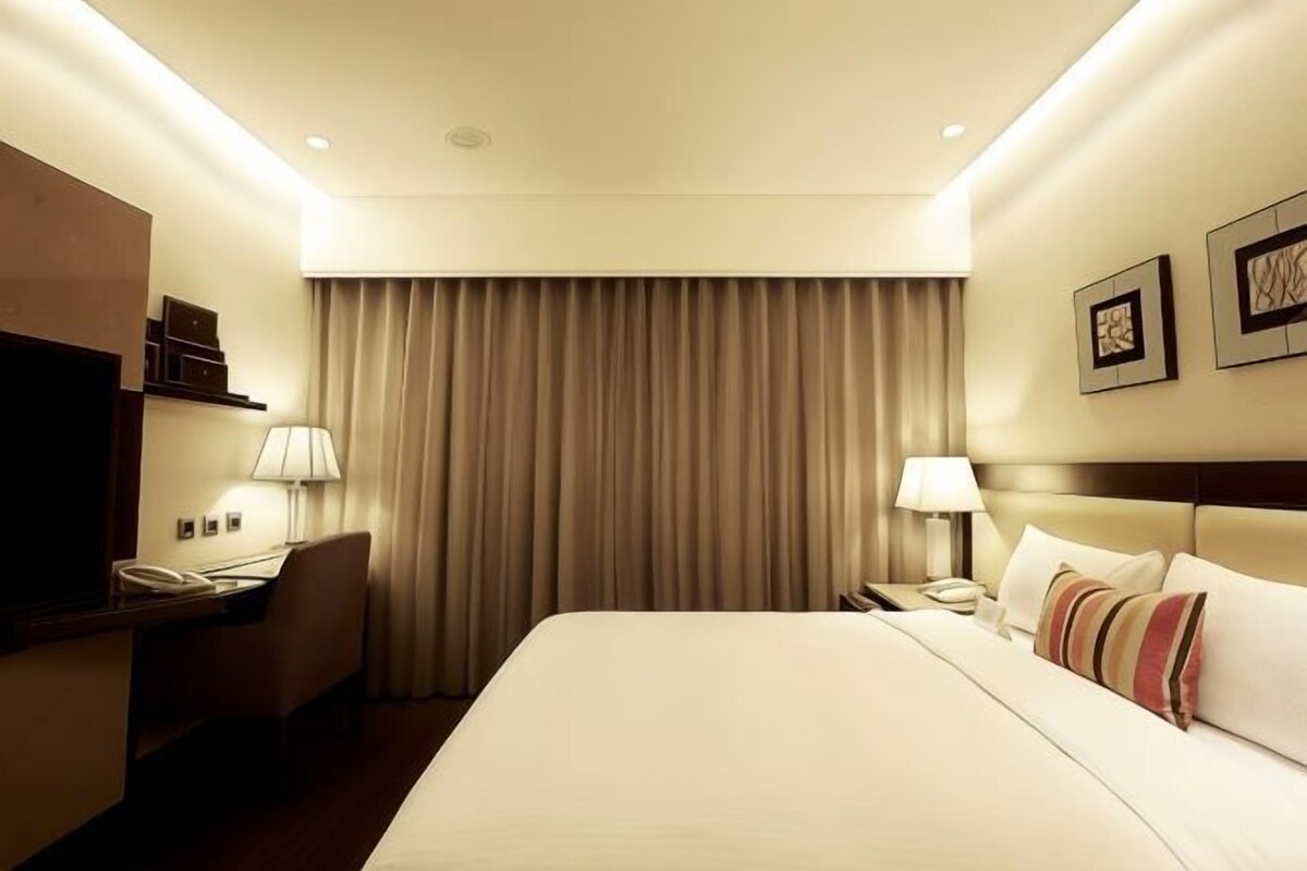 Een hotelkamer met een groot bed, een bureau met telefoon, een lamp en een hoofdeinde met kussens.