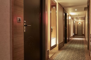 Een hotelgang met houten wanden, een kamerbreed tapijt met dessin en een deur met een paslezer.