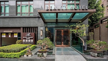 Het uiterlijk van Beauty Hotel, met een moderne gevel, een bord met de tekst Beauty Hotels Taipei, en een verzorgde tuin met bonsaibomen.