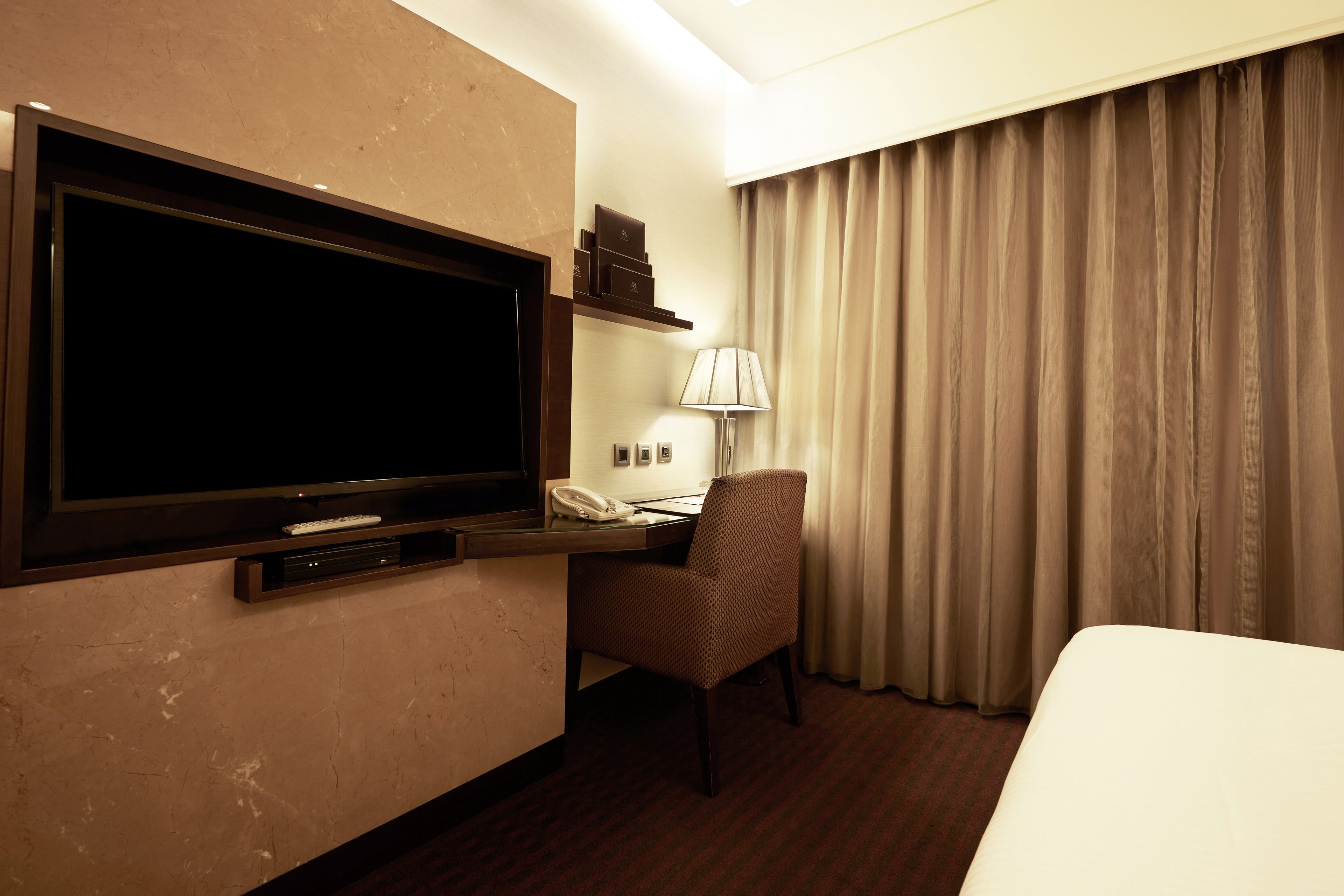 Habitación de hotel con una televisión de pantalla plana grande montada en la pared, un escritorio con lámpara, una silla y una cama.