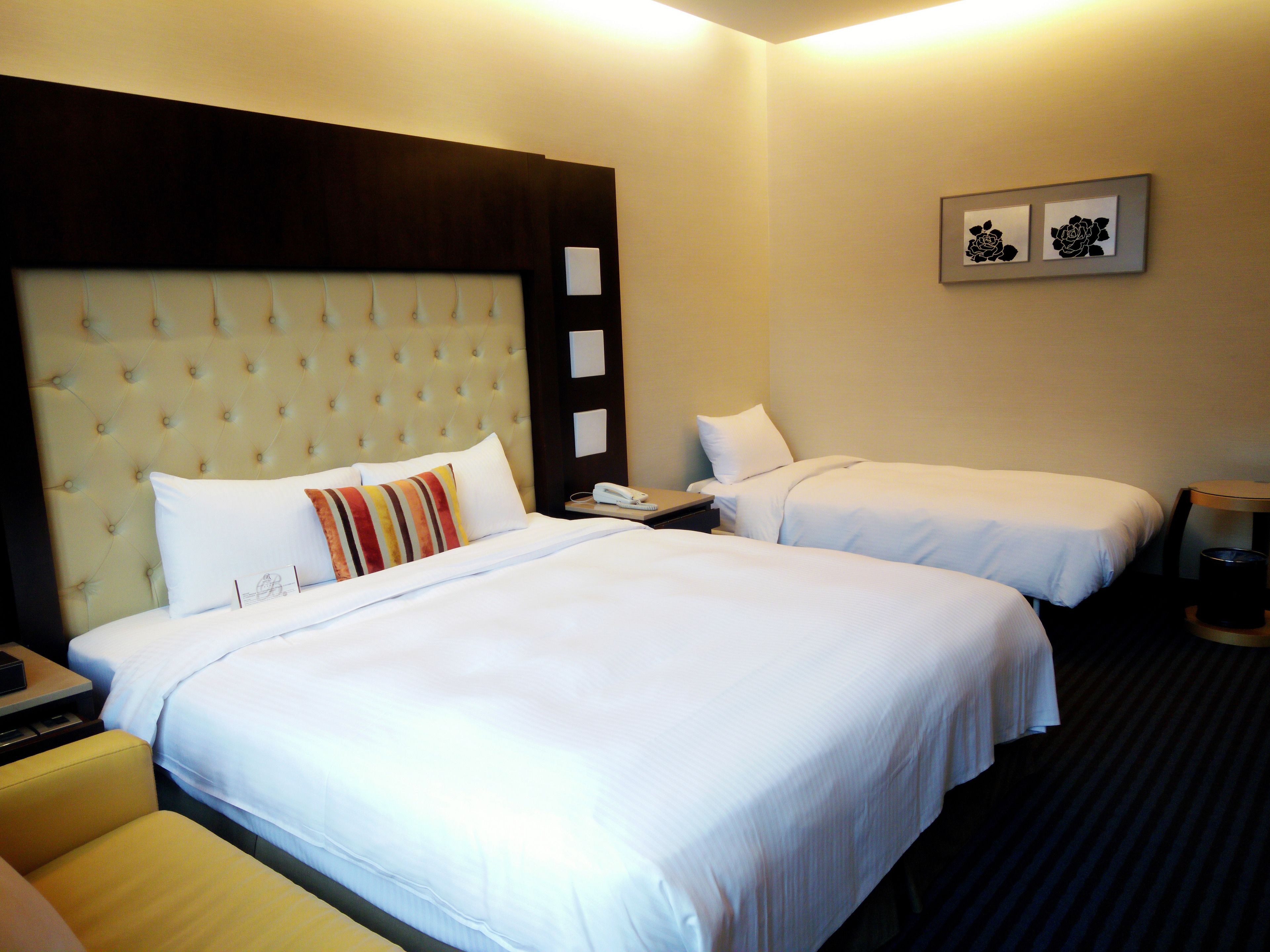 A hotel room with two beds, a nightstand, a lamp, and a trash can.