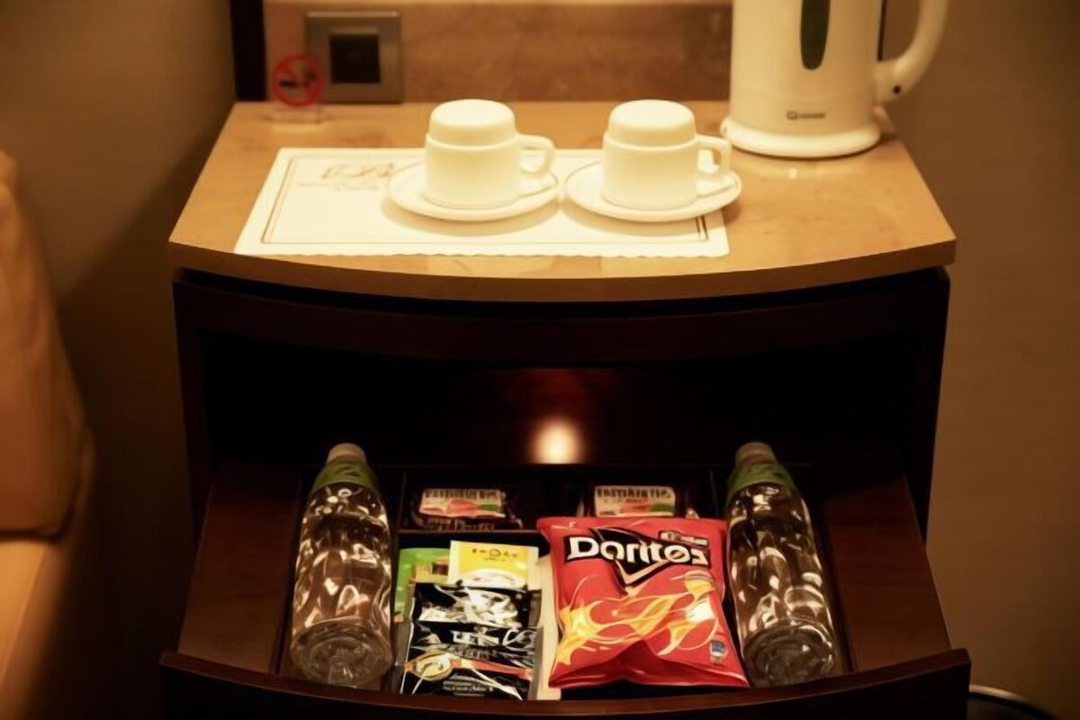 Un mini-bar contenant deux tasses, une bouilloire et des en-cas, notamment des bouteilles d’eau, un paquet de chips Doritos et une boîte de chocolats.