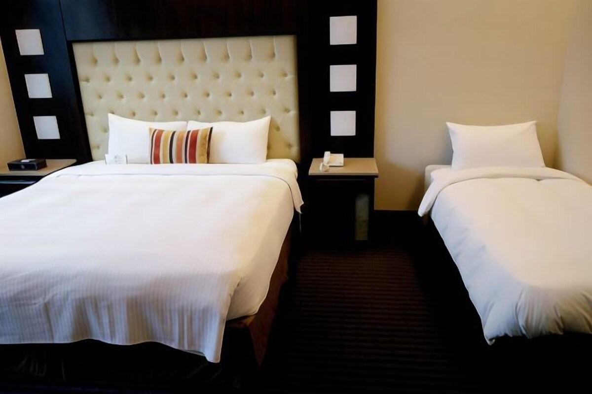 Ein Hotelzimmer mit zwei Betten, einem geprägten Kopfteil, einem Nachttisch mit Telefon und einem dunklen Teppich.